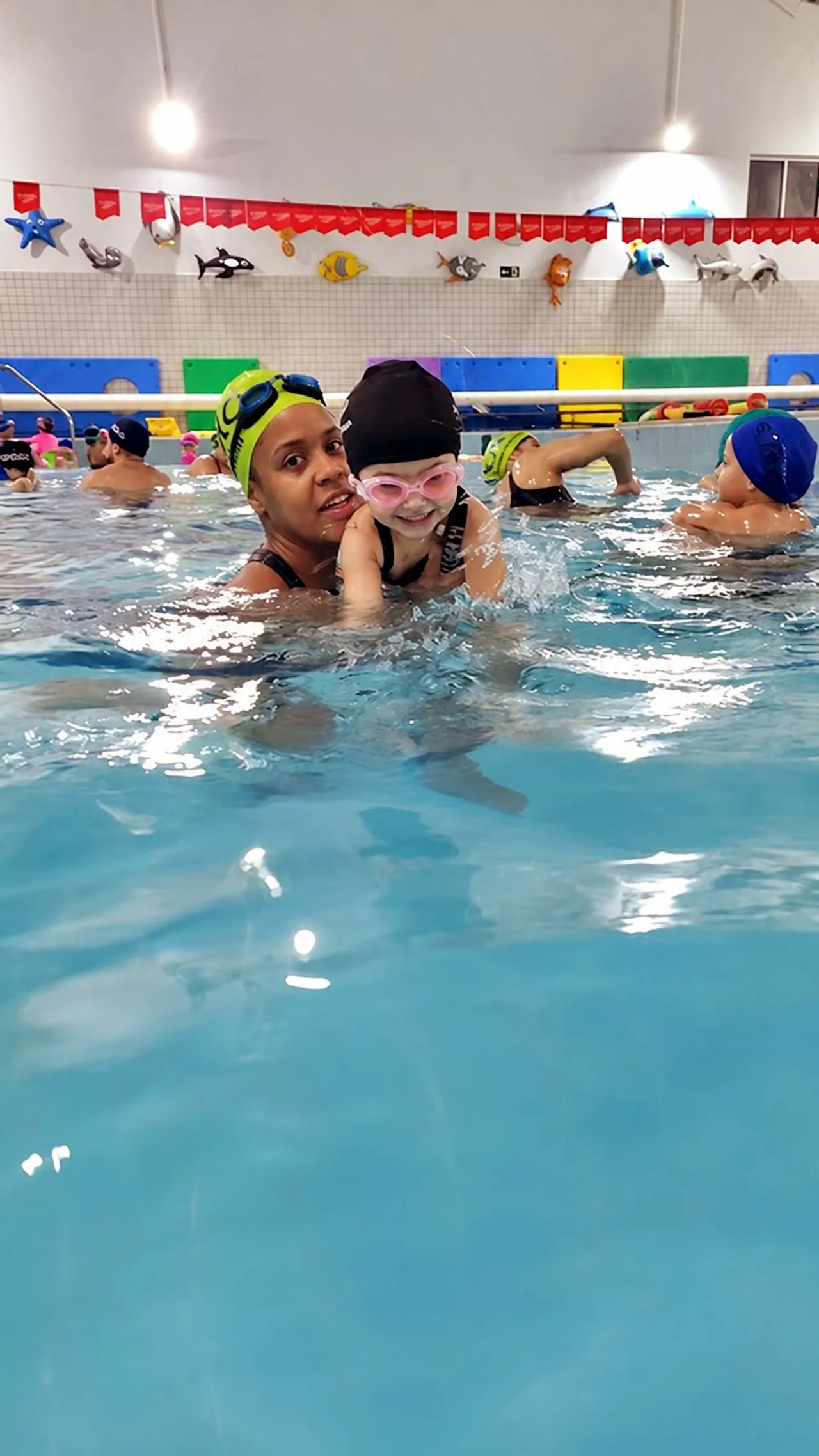 Professora com uma criança de touca e óculos durante a aula de natação infantil